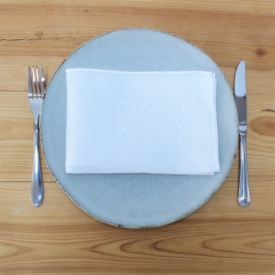 Prato cinza com guardanapo branco e talheres em mesa de madeira clara