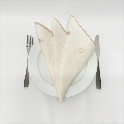 Prato branco com três guardanapos de tecido bege e talheres inox