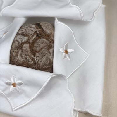 Pano branco bordado com flores envolvendo pão de casca dura escura