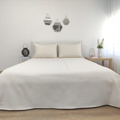 Cama de casal com colcha branca e almofadas, espelhos geométricos na parede e mesas de cabeceira