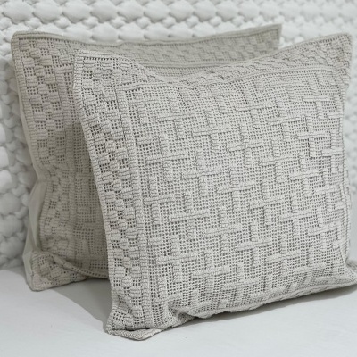 Duas almofadas quadradas bege claro com padrão de malha trançada sobre superfície branca