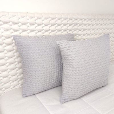 Duas almofadas cinza claro com padrão trançado apoiadas em cabeceira branca com padrão similar