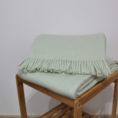 Manta verde claro com franjas sobre banco de madeira clara