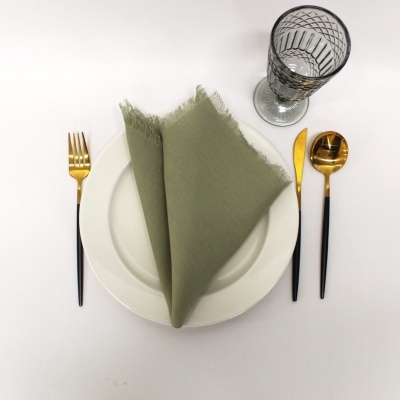 Conjunto de louça branca com guardanapo verde, talheres dourados e copo transparente com padrão preto