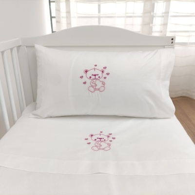 Jogo de cama branco para berço com ursinho bordado cor-de-rosa.