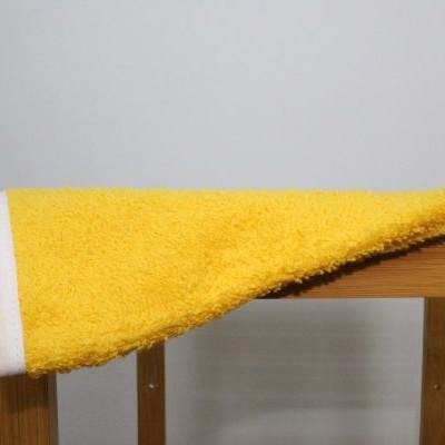 Toalha de banho amarelo com borda branca sobre suporte de madeira