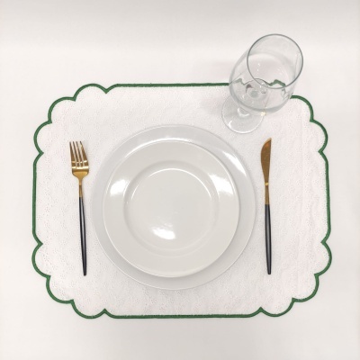 Conjunto de mesa com prato branco, talheres dourados e pretos, copo vidro e individual branco com borda verde