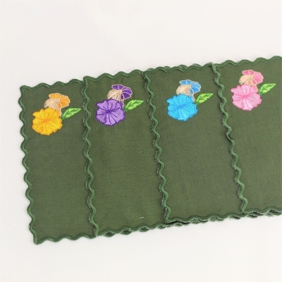 Guardanapos verdes com bordados florais coloridos nas pontas e bordas onduladas