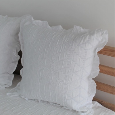 Almofada decorativa branca com padrão em relevo e folho em cabeceira de madeira