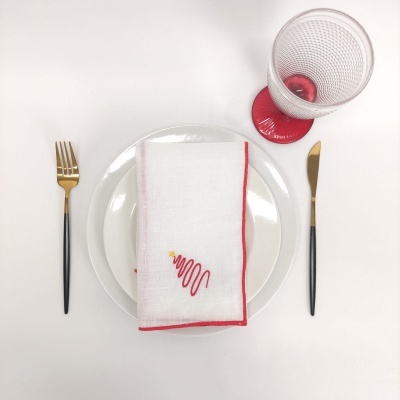 Mesa posta com prato branco, talheres com cabo preto e ouro, guardanapo branco com bordado vermelho e copo transparente com base vermelha