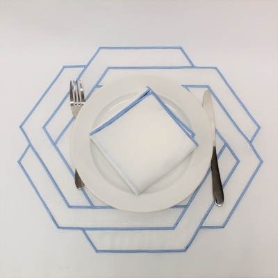 Mesa posta com prato branco, talheres e guardanapo branco com borda azul sobre toalha branca com padrão hexagonal azul