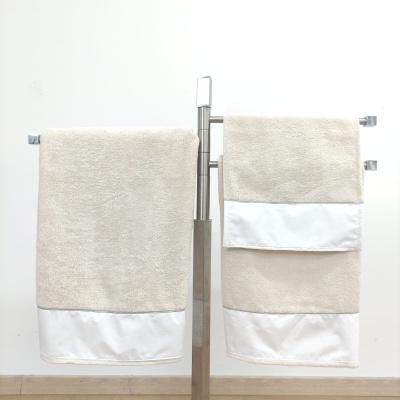 Duas toalhas bege com bordas brancas penduradas num suporte metálico
