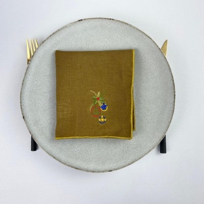 Prato cinza claro com guardanapo verde-oliva bordado no centro, talheres dourados e pretos ao lado