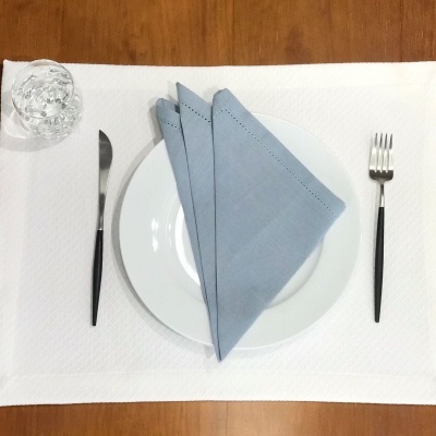 Conjunto de jantar com prato branco, guardanapo azul, talheres pretos e copo de vidro