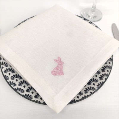 Guardanapo branco bordado com coelho rosa sobre prato decorativo preto e branco