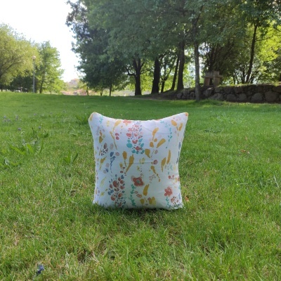 Almofada branca com padrão floral colorido num relvado verde
