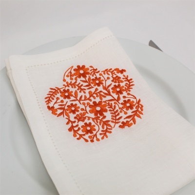Guardanapo branco com bordado floral laranja sobre prato branco