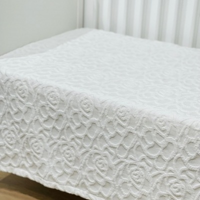 Colcha branca com padrão floral em relevo numa cama branca