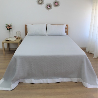 Cama de casal com roupa de cama cinzenta clara e almofadas brancas em quarto minimalista