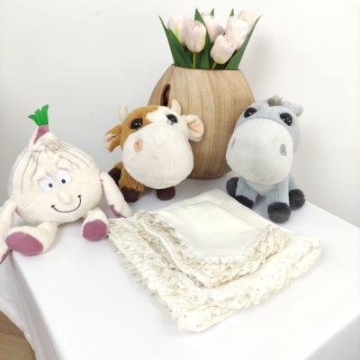 Peluches de legumes e animais com vaso de madeira e guardanapos brancos com renda sobre mesa branca