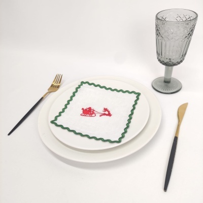 Conjunto de mesa com pratos brancos, guardanapo natalício, talheres pretos e dourados e copo cinza texturizado