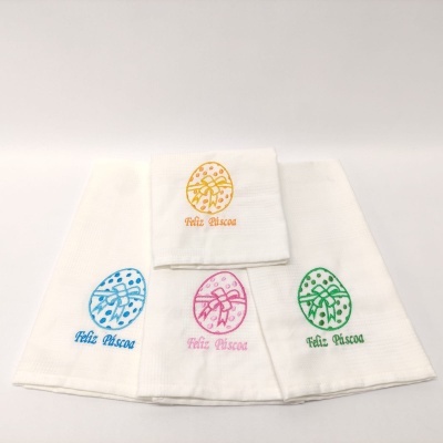 Toalhas brancas com bordados de ovos de Páscoa coloridos e texto Feliz Páscoa.