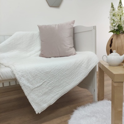 Sofá branco com manta branca e almofada cinza, mesa de madeira com bule e flores