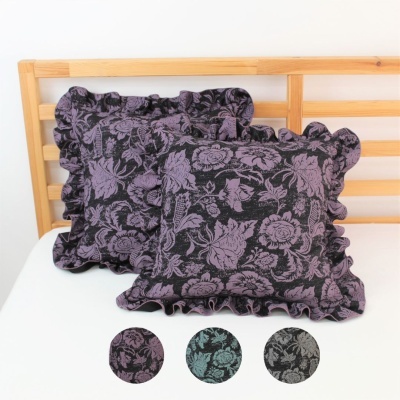 Duas almofadas quadradas pretas com padrão floral lilás e bordas frisadas em cama branca com cabeceira de madeira.