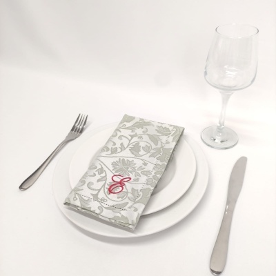 Mesa posta com pratos brancos, guardanapo bordado, talheres de aço inox e copo de vinho transparente