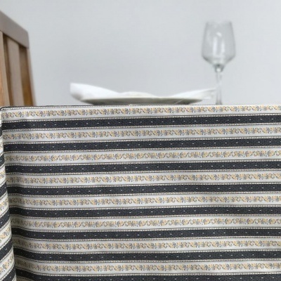 Toalha de mesa com riscas horizontais e detalhes florais dourados sobre mesa com cadeira de madeira