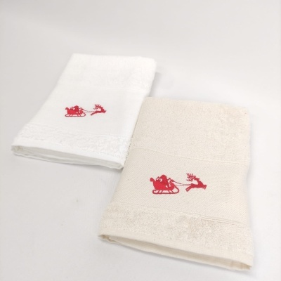 Duas toalhas dobradas, uma branca e outra bege, com bordado vermelho de trenó e rena.