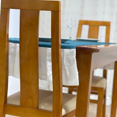 Mesa de madeira com toalha azul e cadeiras de madeira com assentos estofados creme