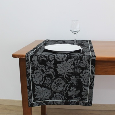Caminho de mesa preto com padrão floral cinzento numa mesa de madeira com prato branco e taça de vidro