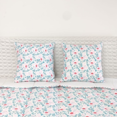 Conjunto de almofadas e cobertura de cama com padrão floral rosa e verde sobre fundo cinza claro.