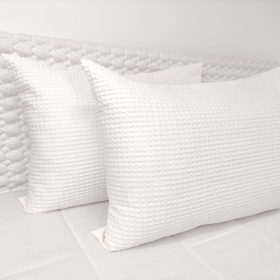 Duas almofadas brancas texturizadas sobre uma cama branca.
