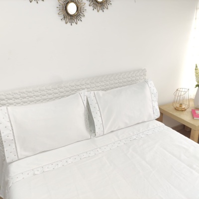 Cama branca com lençóis bordados e mesa de cabeceira de madeira clara com decoração