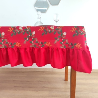 Toalha de mesa vermelha com padrão floral e folho sobre mesa de madeira clara