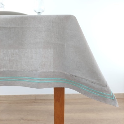 Toalha de mesa cinza clara com linhas verdes na bainha sobre mesa de madeira