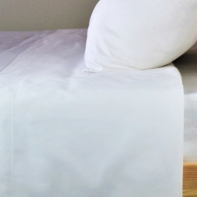 Cama de madeira clara com roupa de cama branca.