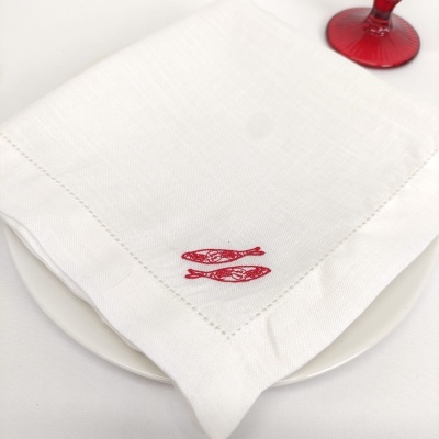 Guardanapo branco com bordado de peixes vermelhos sobre prato branco