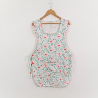 Avental de cozinha branco com padrão floral verde e flores cor-de-rosa pendurado num cabide de madeira