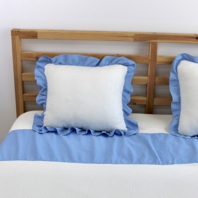 Almofadas brancas com folhos azuis numa cama com cabeceira de madeira