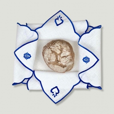 Guardanapo branco com bordado azul e pão redondo no centro