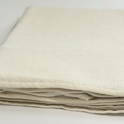 Manta bege clara dobrada com textura geométrica sobre superfície branca.