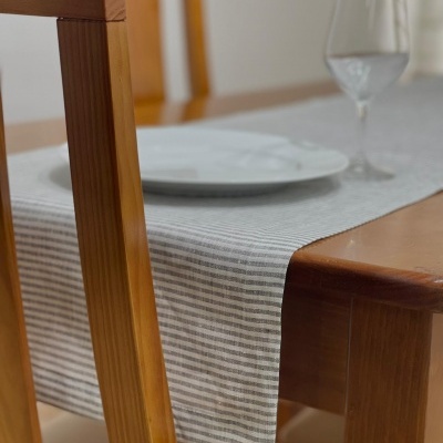 Mesa de madeira com toalha de mesa cinza riscada, prato branco e copo de vidro