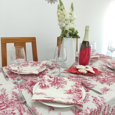 Mesa de jantar com toalha branca e vermelha, pratos, copos, talheres, vaso branco com flores e garrafa de champanhe