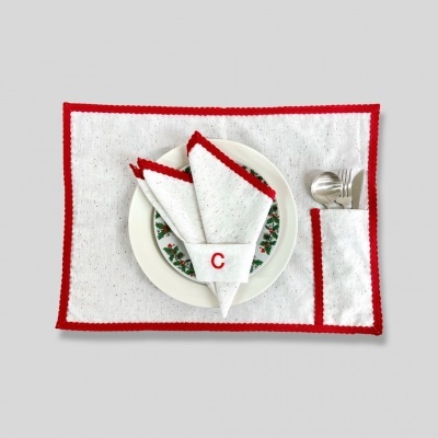 Jogo americano branco com borda vermelha, guardanapo com borda vermelha e letra C, prato decorado, talheres metálicos ao lado