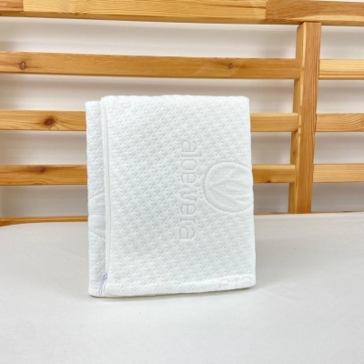 Colchão viscoelástico branco com padrão em losangos e logo em relevo sobre mesa