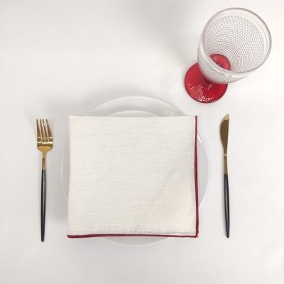 Serviço de mesa com pratos brancos, talheres dourados e pretos, guardanapo branco com borda vermelha e copo com base vermelha