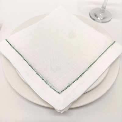 Guardanapo branco com bordado verde sobre prato branco e taça ao lado